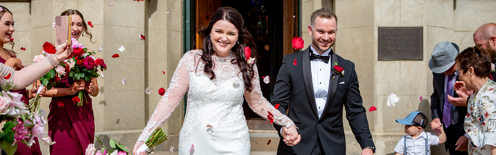 930476b0-4043-4e42-a4eb-e8a70893399a-celebrant jey and matt emerge from church in triumph and rose petals.png